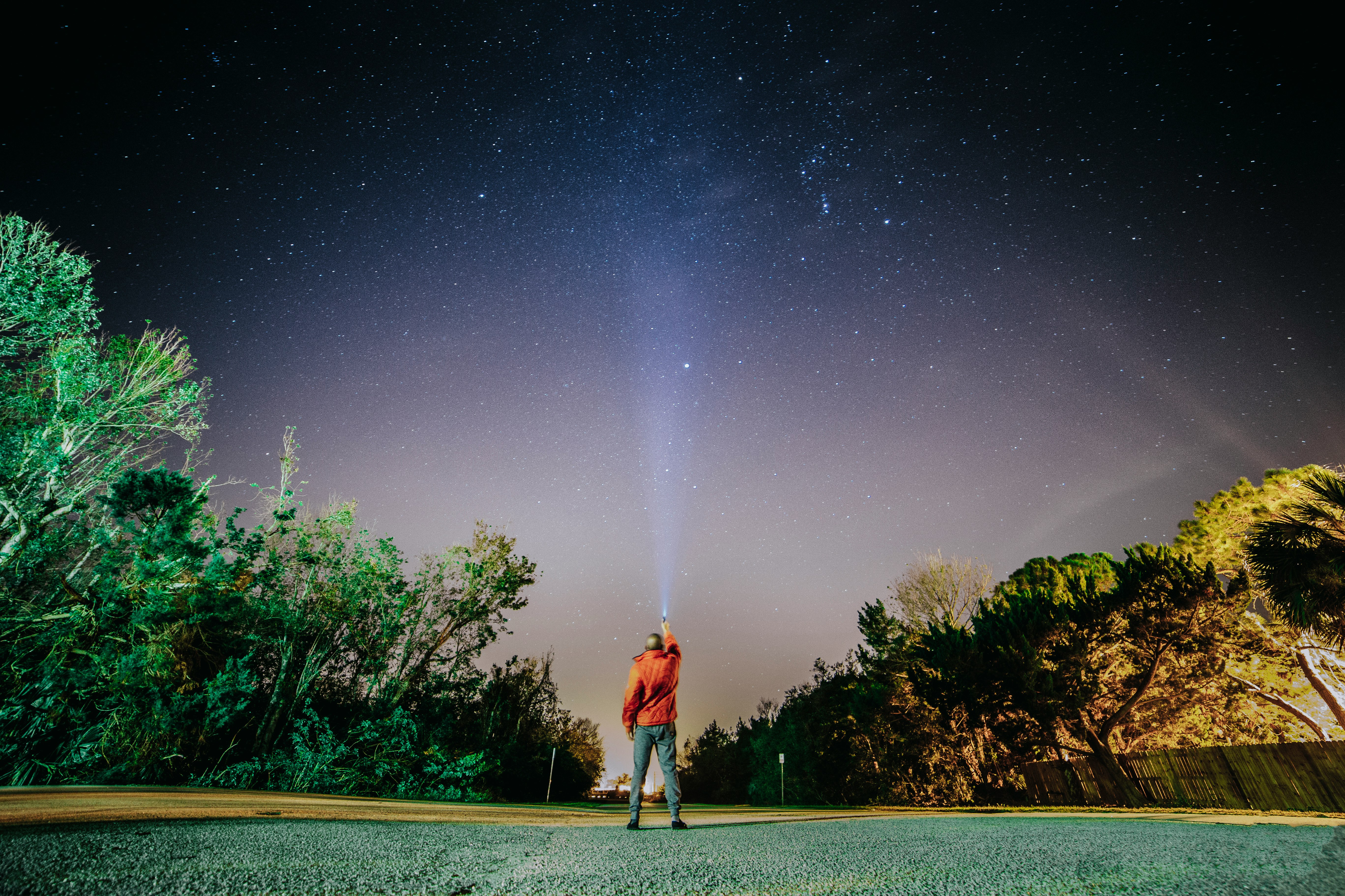 man in red shirt standing on gray concrete pathway under starry night